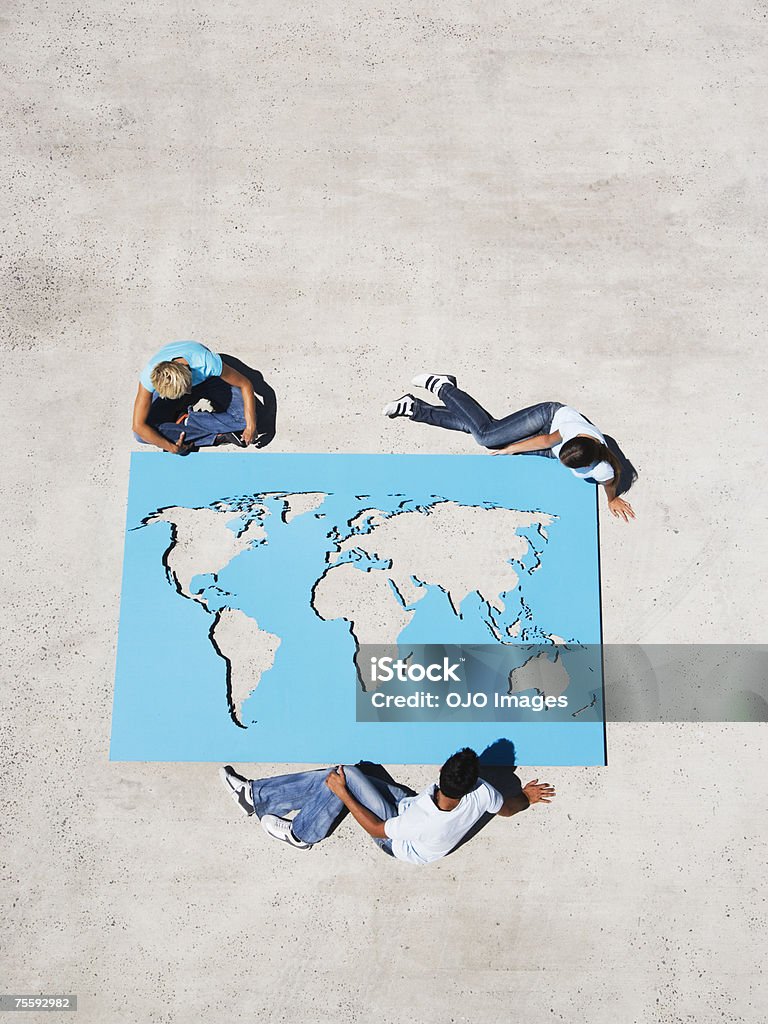Vista aérea de tres personas mirando hacia abajo en mapa mundial - Foto de stock de 25-29 años libre de derechos