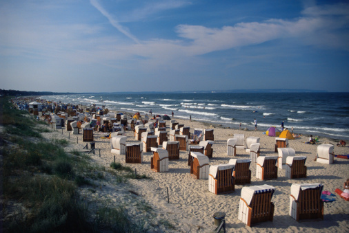 White traditional wicker beach baskets on the sandy beach at the Baltic Sea, with wooden breakwater in the sea and blue sky on the island of Poel, Germany