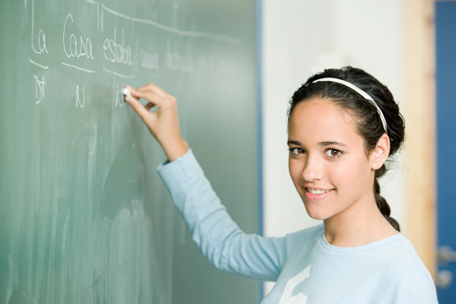 student woman or teacher in the class writes math formulas in chalk on a black chalkboard. young girl stands with her back to the camera. Back to school. Education concept. Banner. Place for your text