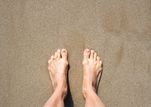 Close up of woman feet laying on white sand beach with blue sky and shining sun at background. Copy space.