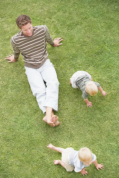 Photo of Man with two babies crawling on grass