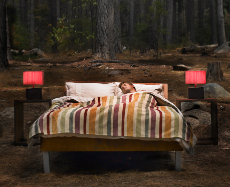 A man sleeping in a bed outdoors in the woods