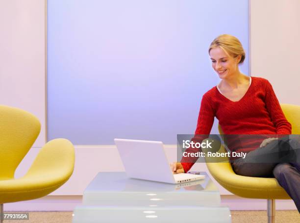 Photo libre de droit de Femme Assise Dans Un Fauteuil En Regardant Un Ordinateur Portable banque d'images et plus d'images libres de droit de Bureau - Lieu de travail