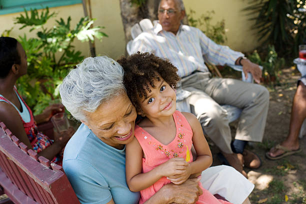 mujer abrazar chica joven con personas en el fondo - grandmother generation gap senior adult granddaughter fotografías e imágenes de stock