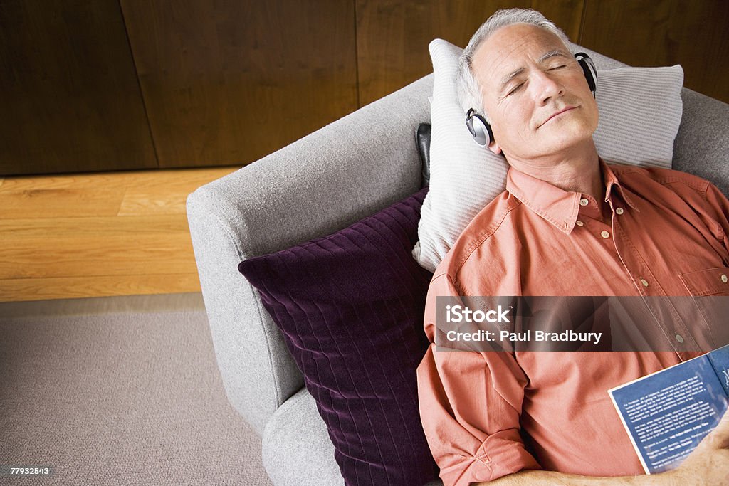 Человек носить наушники, спать на диване с книги - Стоковые фото 55-59 лет роялти-фри