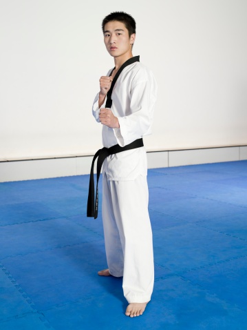 Portrait of a taekwondo athlete standing at martial art school in strike position and smiling at the camera.