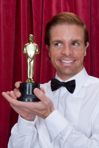 Stylish young blond man in a tuxedo holding a microphone, posing against a dark background with smoke