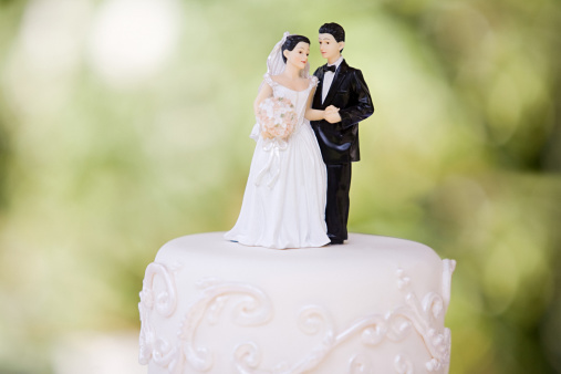 Shot of a cake topped with plastic bride and groom figurines at an outdoor wedding