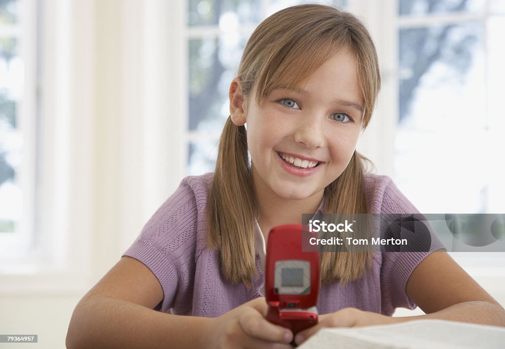 Jeune fille avec téléphone mobile et faire ses devoirs au kitchen table - Photo de Faire ses devoirs libre de droits