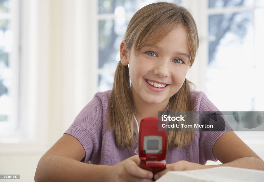 Młoda dziewczyna z telefonu komórkowego i pracę domową w kitchen table - Zbiór zdjęć royalty-free (Budynek szkolny)