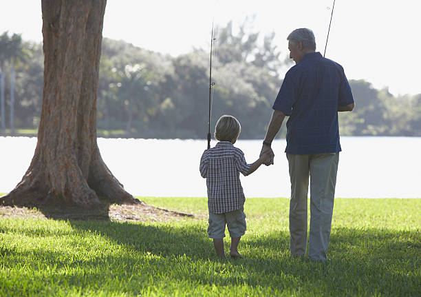 homme et jeune garçon pêche avec des bâtons en plein air au parc - fishing lake grandfather grandson photos et images de collection