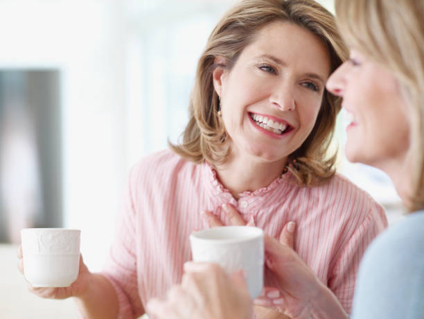 dos mujeres en el interior de retención, tazas y hablando - coffee buzz fotografías e imágenes de stock