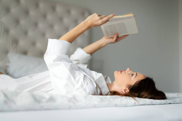 istock Young woman at home on bed reading book 800001064