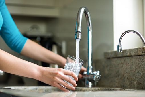 Pretty blonde woman filling a glass of water at home