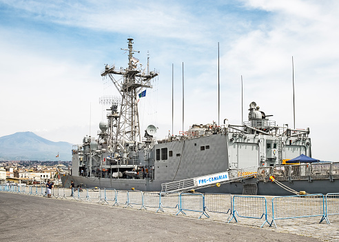 Catania, Italy - May 15, 2017: Rear side view of the naval frigate F86 - CANARIAS in dock at the Catania commercial harbor in Catania, Italy. In the background left the active volcano Mount Etna.