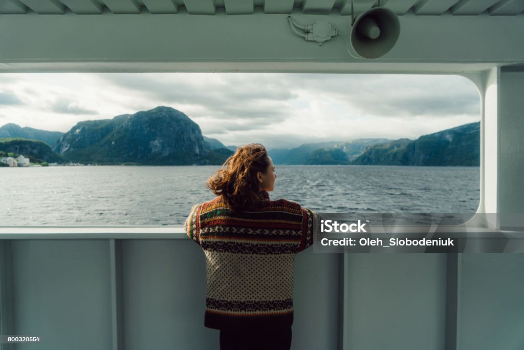 Woman looking at scenic view from ferry Young Caucasian woman  in knitted sweater looking at scenic view from ferry in Norway Norway Stock Photo