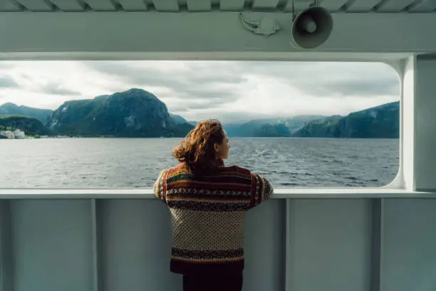 Young Caucasian woman  in knitted sweater looking at scenic view from ferry in Norway