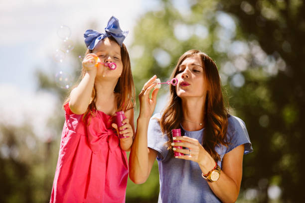 istock Mom and daughter blowing bubbles in the park 800334640