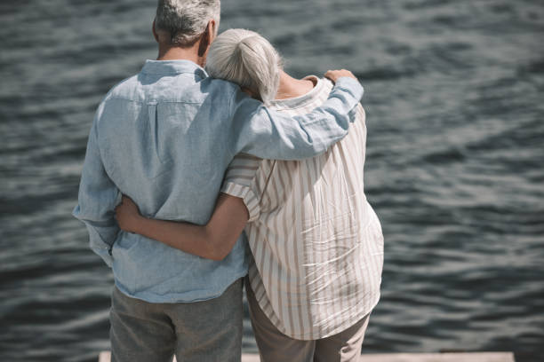 istock Back view of elderly couple standing embracing and looking at waves 800342008