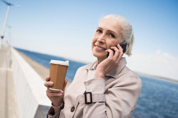 istock smiling elderly woman talking on smartphone and holding coffee cup at quay 800349034