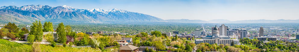 Blue skies and snow capped mountains above the landmarks of Salt Lake City, from the leafy suburbs and University campus to the monumental dome of the State Capitol and the ornamental spires of the Mormon Temple surrounded by the skyscrapers of downtown, Utah, USA.