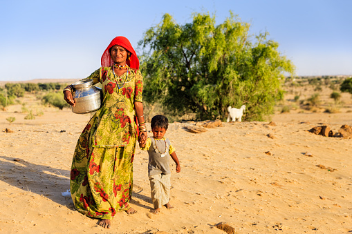 Indian woman carrying water to the village. desert village, Rajasthan, India. Potable water is very precious on the desert - Rajasthani women and children often walk long distances through the desert to bring back jugs of water that they carry on their heads.