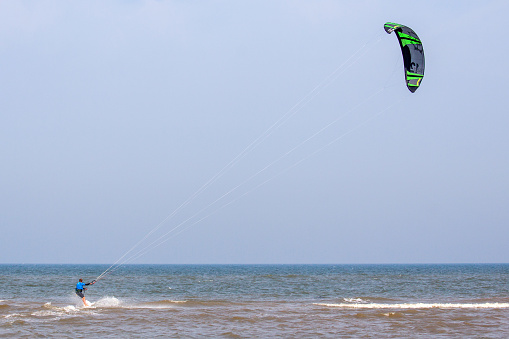 A wide-angle shot captures the serenity and excitement of kite surfing, as a skilled surfer rides the waves, framed by the vastness of the open sea.