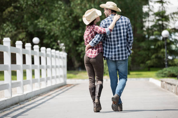 back view of cowboy with his girlfriend walking on pathway in park at daytime