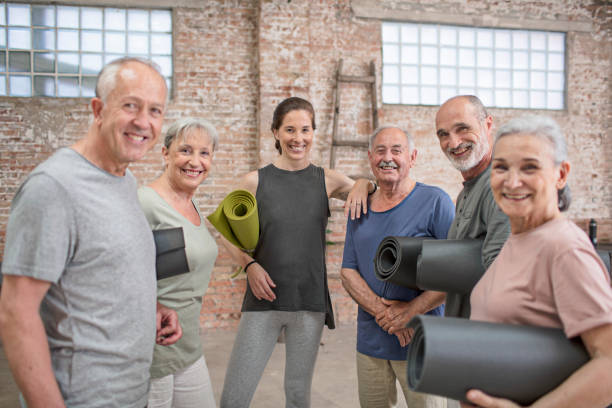 ausbilder mit fröhlichen senior menschen in yoga-kurs - senior adult exercising aging process instructor stock-fotos und bilder