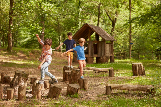 amigos que juegan sobre tocones de árboles en bosque - three boys fotografías e imágenes de stock