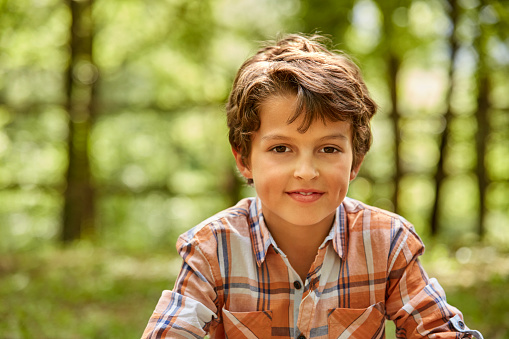 Portrait of cute boy against trees. Smiling male is wearing orange shirt. He is relaxing in forest.