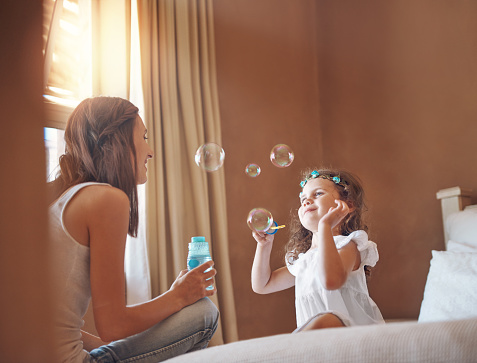 Shot of a mother and her little daughter playing with bubbles at home