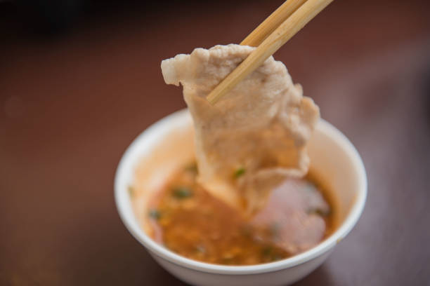 Hand holding pork using chopsticks and sauce shabu .