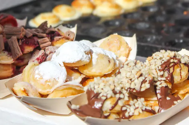 Close up of Sweet Dutch pancakes (poffertjes) with different variation of toppings, from sugar powdered , until chocolate peanut sauce.