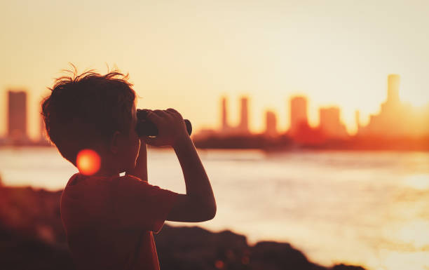 little boy looking at sunset city through binoculars, travel concept