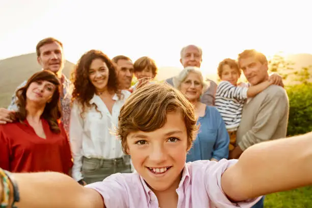 Portrait of smiling boy against family. Close-up of happy male with people in background. They are having leisure time in yard.