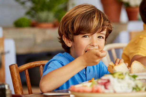 portrait of boy eating food at table in house - childrens food foto e immagini stock