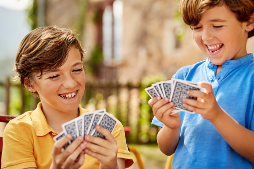 Happy boys playing cards in yard. Siblings enjoying leisure games. They are wearing casuals.