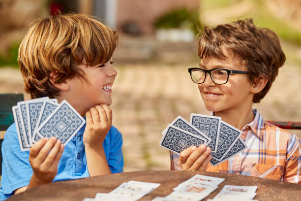 hermanos sonrientes jugando a las cartas en la mesa en el patio - game cards fotografías e imágenes de stock