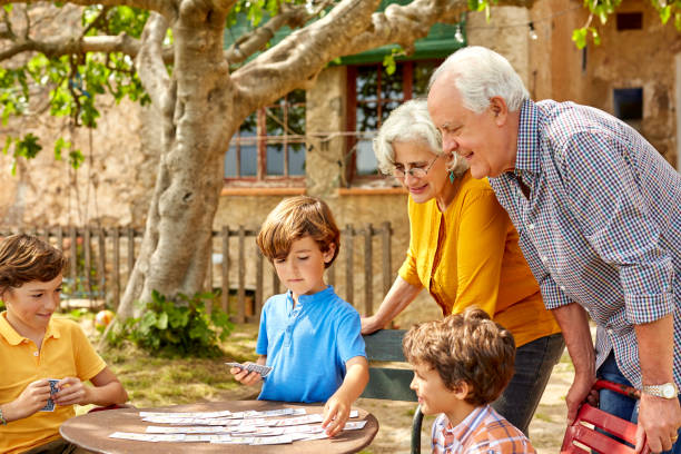 Grandparents looking at children playing card Grandparents looking at children playing cards. Playful boys with senior couple in yard. They are wearing casuals. family playing card game stock pictures, royalty-free photos & images