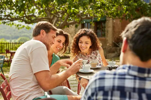 Man showing mobile phone to female friends. People are enjoying coffee in yard. They are having leisure time.