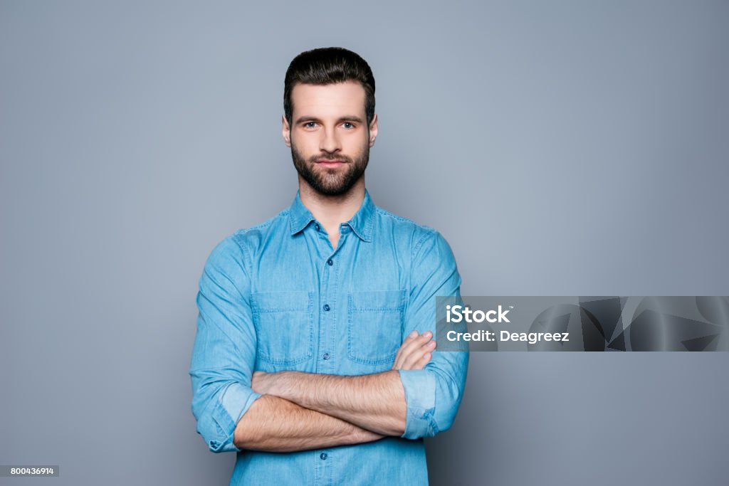 Um retrato da jovem sorridente bonito no pé de camisa jeans com as mãos cruzadas - Foto de stock de Homens royalty-free