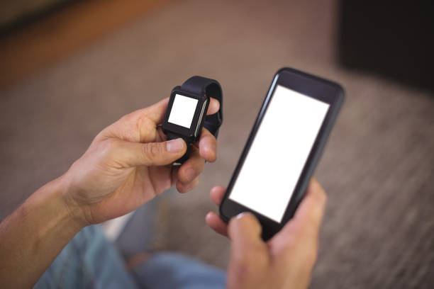 Close-up of man using smart watch and mobile phone in living room