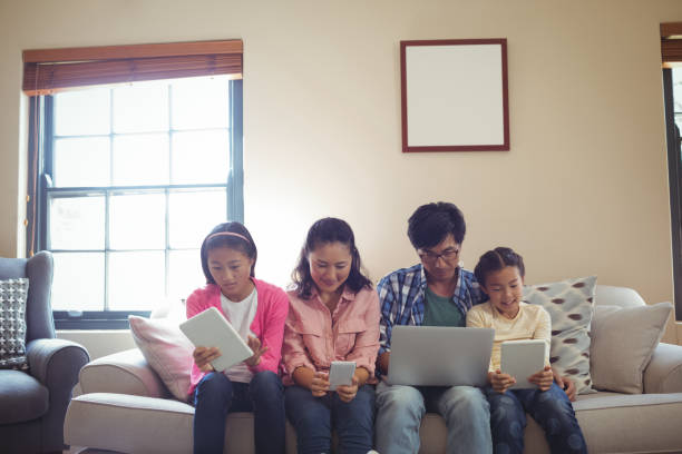 family using laptop, digital tablet and mobile phone in living room - father digital tablet asian ethnicity daughter imagens e fotografias de stock