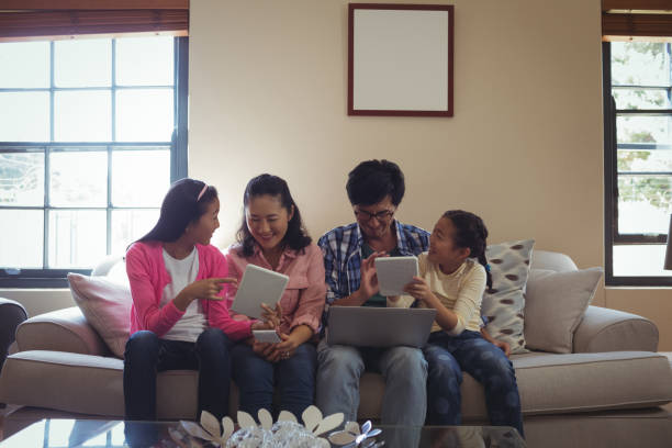 family using laptop, digital tablet and mobile phone in living room - father digital tablet asian ethnicity daughter imagens e fotografias de stock