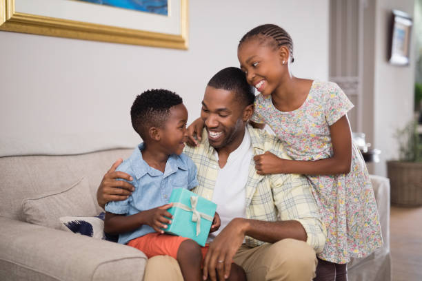 istock Father and children holding gift box on sofa at home 800475840