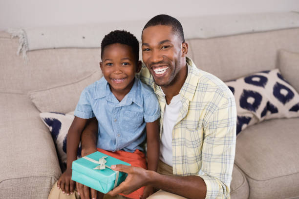 istock Smiling father and son with gift box sitting on sofa at home 800475954