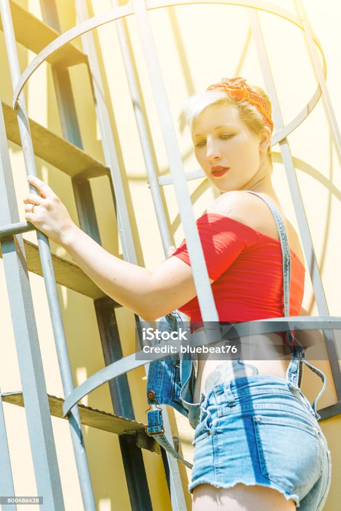 Young blonde pinup girl with a red bow on a emergency stairway. Concept pinup woman. Adult Stock Photo