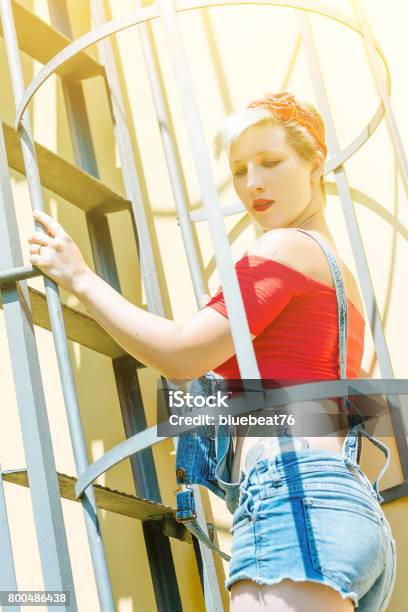 Young Blonde Pinup Girl With A Red Bow On A Emergency Stairway Concept Pinup Woman Stock Photo - Download Image Now