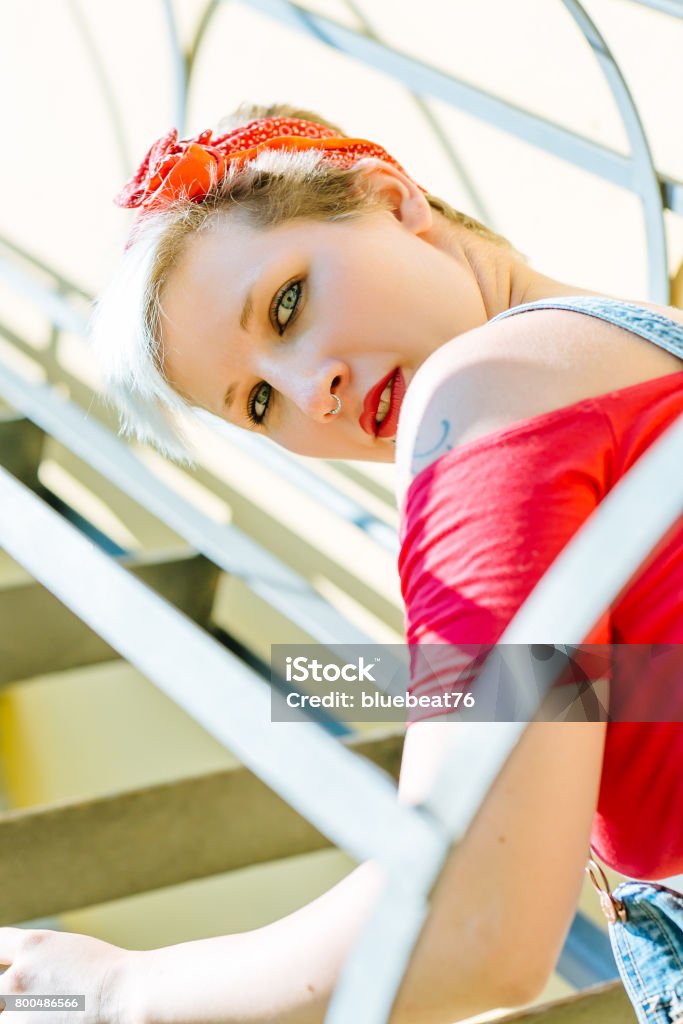 Young blonde pinup girl with a red bow on a emergency stairway. Concept pinup woman. Adult Stock Photo